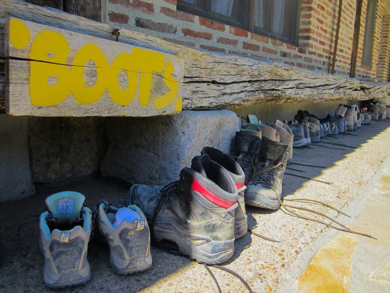 Das Foto zeigt einige aufgestellte Wanderschuhe vor einer Herberge draußen